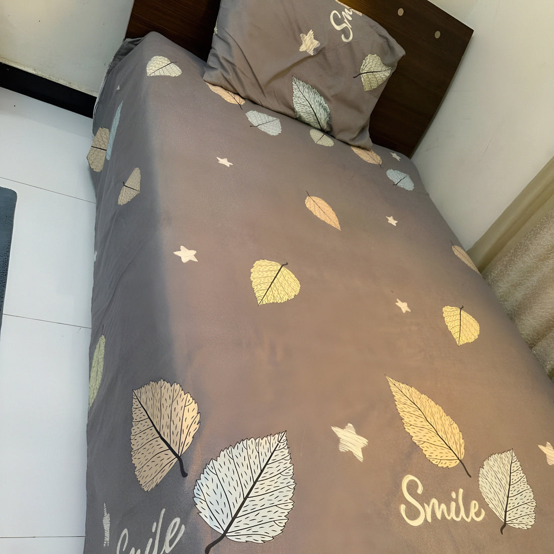 Luxury grey bedsheet with leaf print and “Smile” lettering, styled neatly on a single bed — Marjan3x home decor collection UAE.