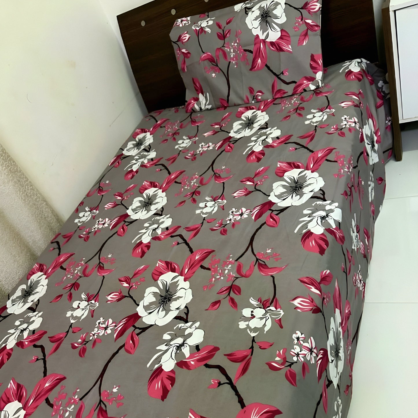 Pink floral bedsheet with white blossoms on grey background, styled on a single bed — Marjan3x UAE